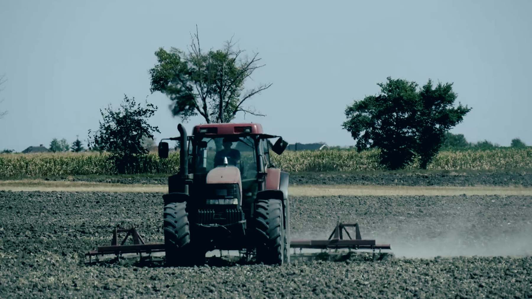 A tractor working a field, dust behind the harrow.